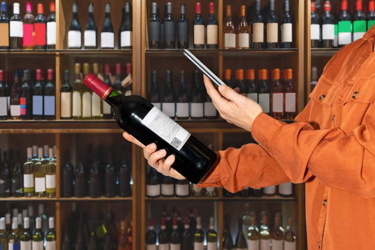 Consumer in Wine Shop scanning data matrix QR code on label of wine bottles using mobile phone. NFC and RFID technology in alcohol industry.