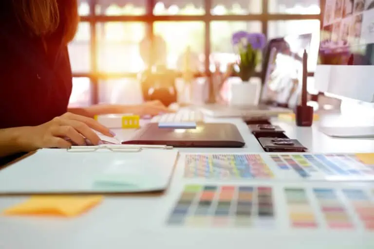 Designer looking through colour samples at her desk with a graphics tablet and mac in front of her